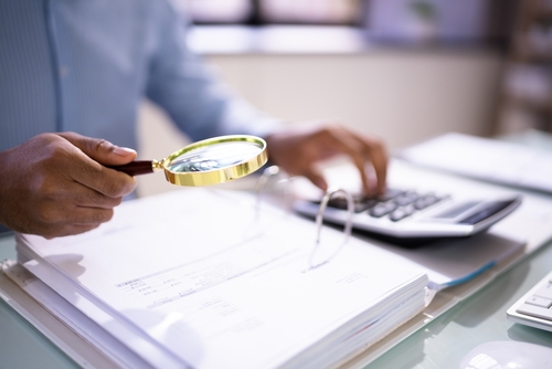 Picture of someone with a magnifying glass looking thru a book of papers for a Fixed Percentage Option to resolve Medicare conditional payments liability settlements of up to $10,000.